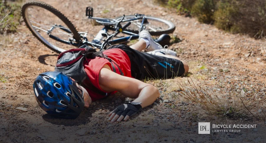 A cyclist wearing a blue helmet lies face down on a dirt trail after a crash.
