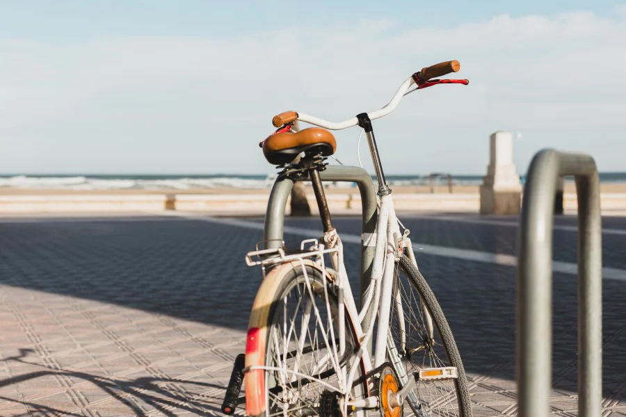A white vintage bicycle parked at a beach boardwalk rack overlooking the ocean on a sunny day.
