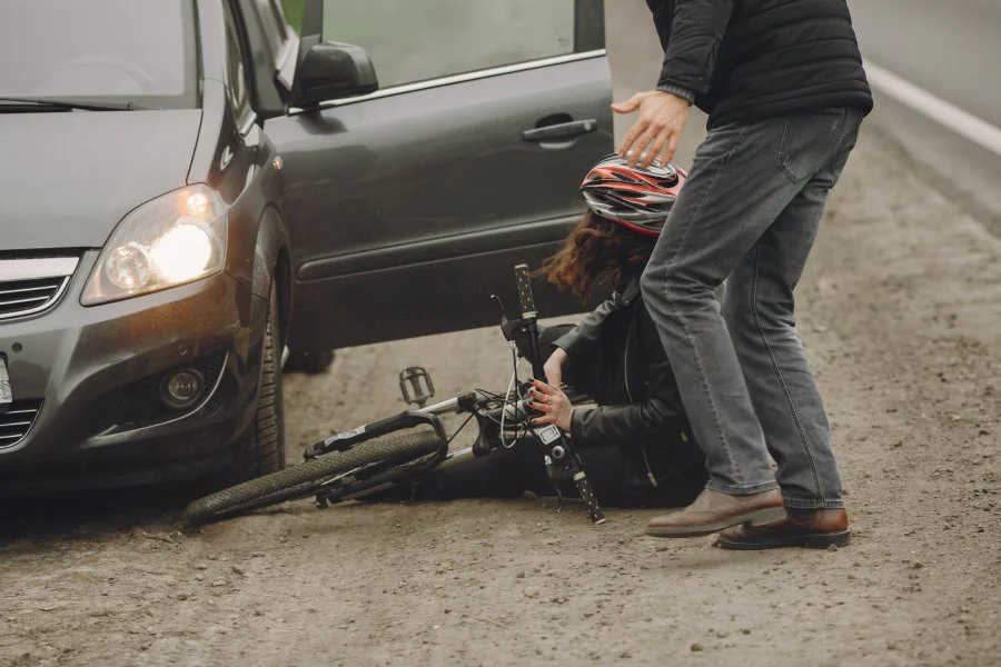 A cyclist sits on the ground with her bike after an accident with a car.