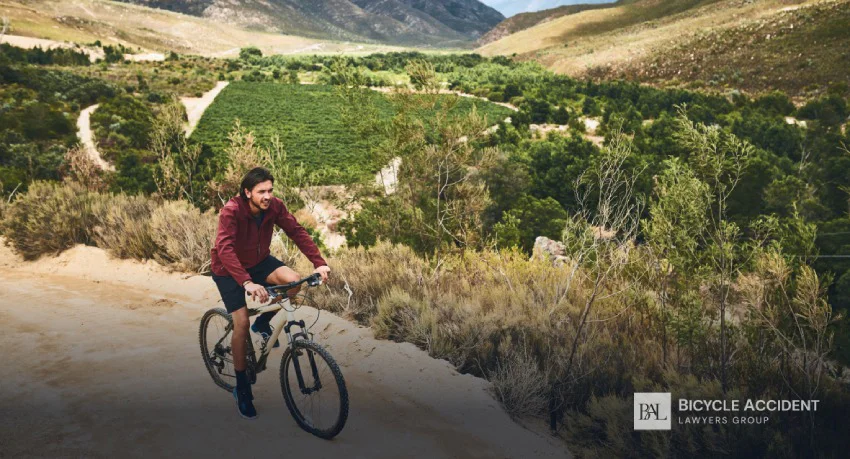 A man in a red jacket rides his mountain bike along a winding trail overlooking a lush valley.
