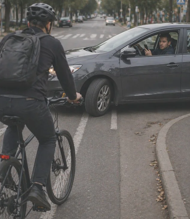 Driver using phone turns across cyclist’s path at intersection, creating collision risk.