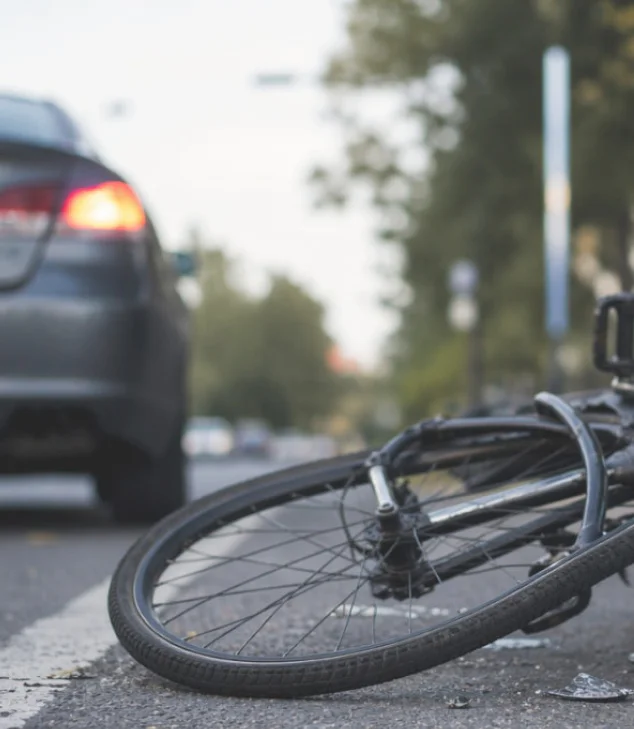 Bicycle lying on road near car after collision, debris scattered on pavement.