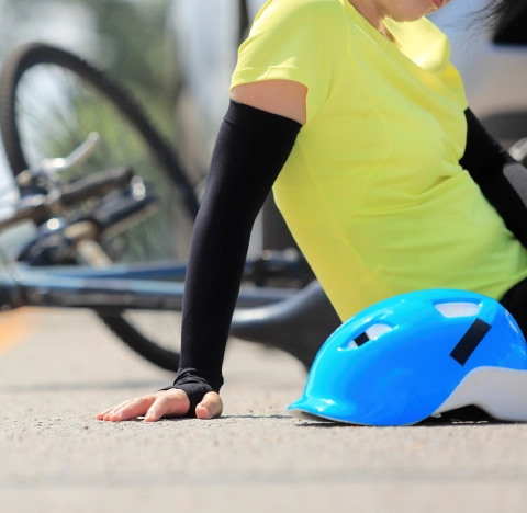 Injured cyclist sitting on the road beside a fallen bicycle and helmet.